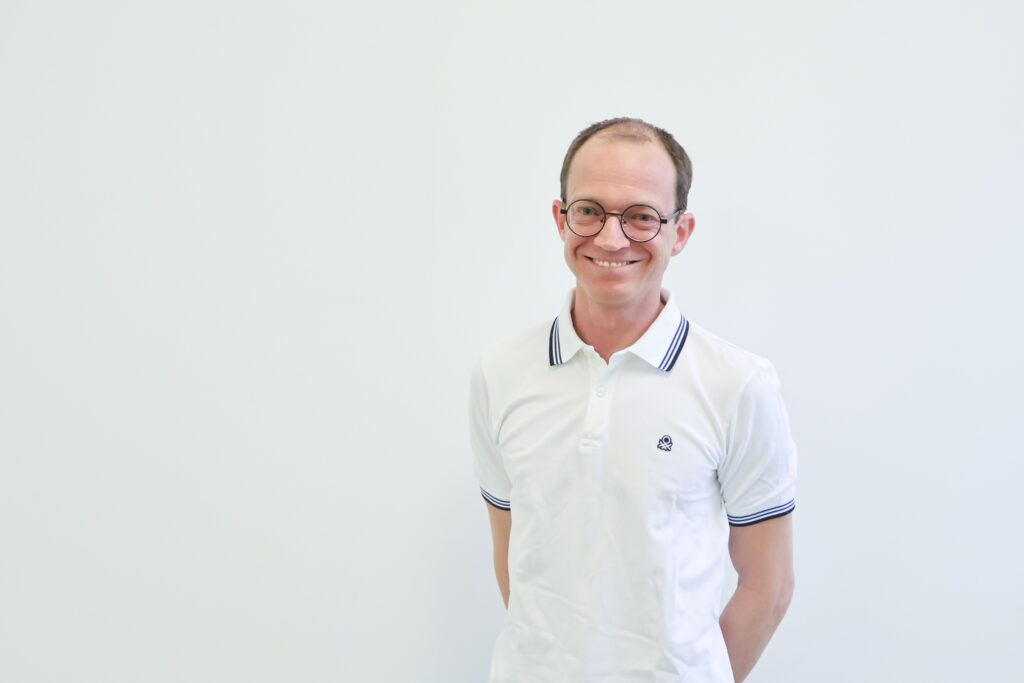 ||Portrait Raphael Stehrer|Ein Mann steht vor einer weißen Wand|Ein Mann steht vor einer weißen Wand und lächelt