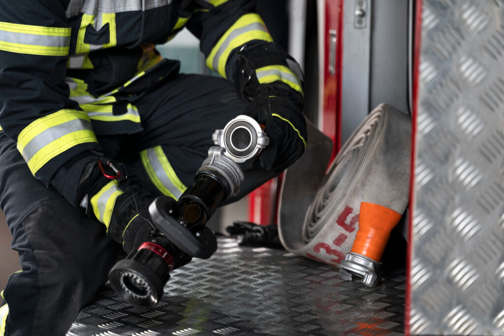 Du siehst den OberkÃ¶rper und die Beine einer Person in der Feuerwehruniform die eine Schlauchkupplung in der Hand hÃ¤lt.