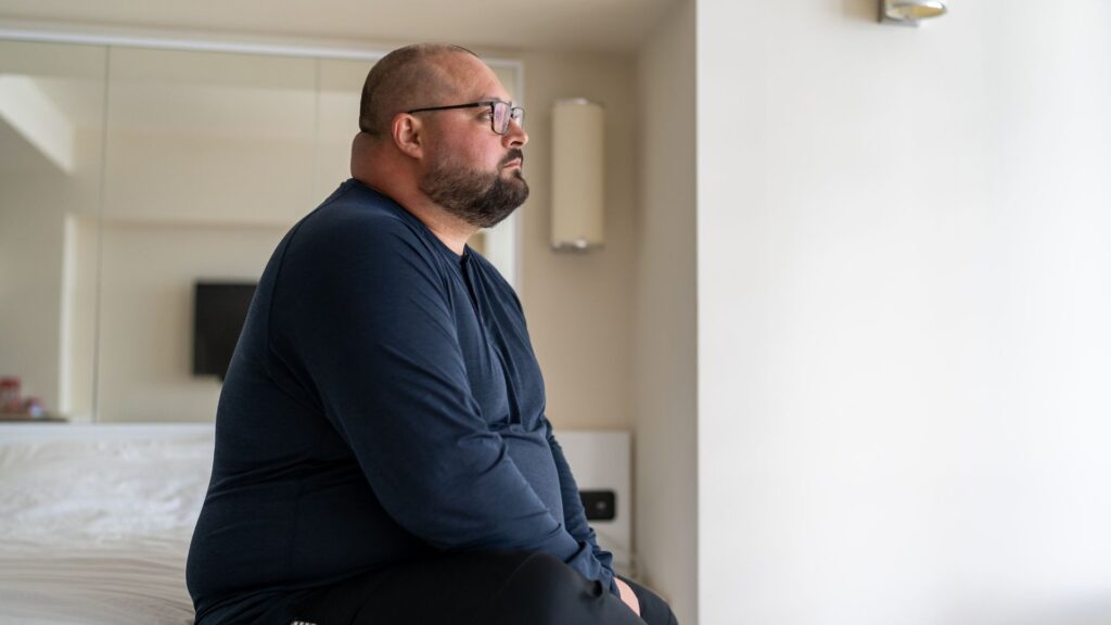 Ein Ãbergewichtiger Mann sitzt auf einem Bett
